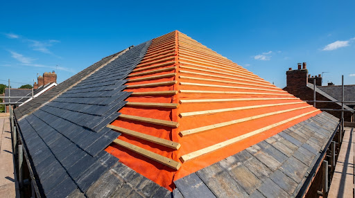 Fresh slate roof with bright orange breather membrane and timber battens under a clear blue sky.